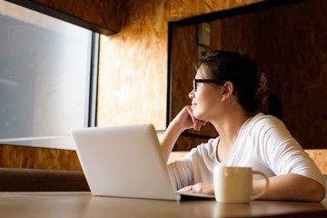 Asian woman thinks about her project with laptop in coffee shop