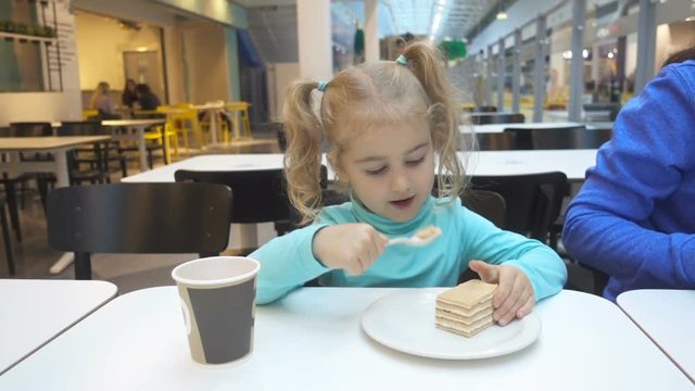 Little girl child eats in a cafe. Baby girl sitting at a table in a cafe and eating a piece of cake.
