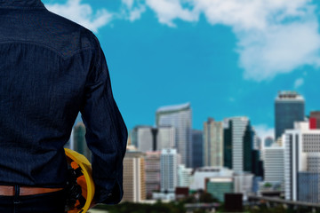 Hand's engineer worker holding yellow safety helmet with blurred city and blue sky