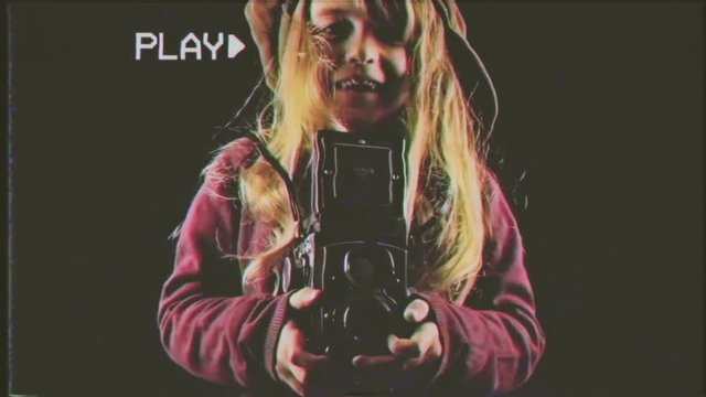Fake VHS tape: a cute little girl enjoying taking photos like a paparazzo (a stereotyped celebrities' photographer) with a vintage film camera.
