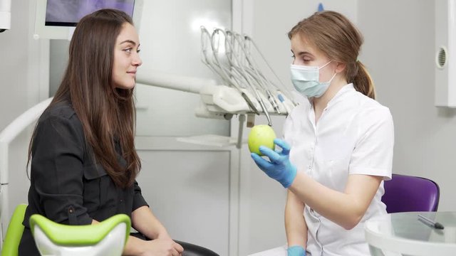 Young female dentist offering green apple to happy and healthy patient after the procedures