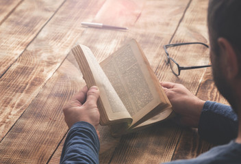 Man reading book sitting at a wooden table