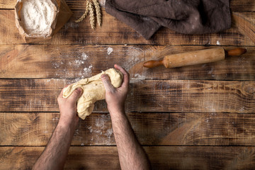 Male hands knead the dough on a wooden table