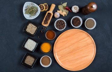 Indian spices, herbs and empty round cutting board on black background