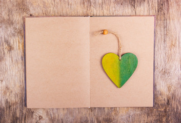 An open book with empty sheets and a wooden bookmark. Wooden pendant in the shape of heart. Copy space.