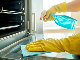 Man's hand in glove with rag cleaning oven