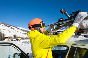 Male skier fastening skis to roof rails of car