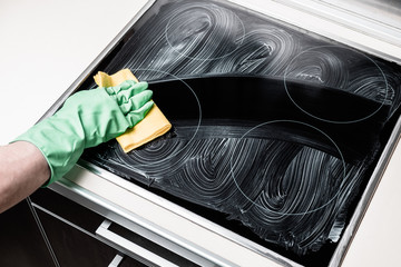Man's hand in green glove cleaning cooker at home kitchen