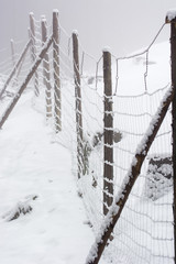 Wooden posts with a wire fence with big holes in winter with snow.