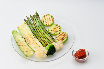 Grilled zucchini and asparagus, broccoli and cauliflower on a glass plate with red sauce