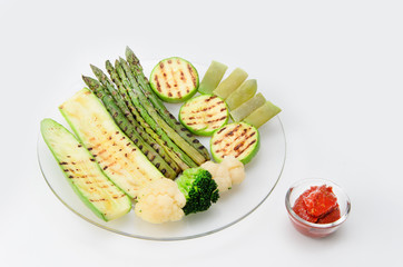 Grilled zucchini and asparagus, broccoli, lobi and cauliflower on a glass plate with red sauce