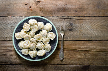 Fototapeta na wymiar Boiled prepared homemade russian pelmeni, dumplings, ravioli with meat on grey plate with fresh parsley, pepper, wooden rustic background. Top view. Copyspace
