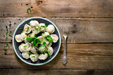 Boiled prepared homemade russian pelmeni, dumplings, ravioli with meat on grey plate with fresh parsley, pepper, wooden rustic background. Top view. Copyspace