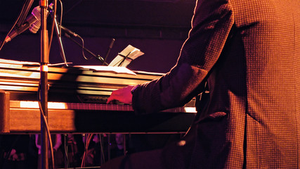 Piano player plays the piano keyboard on the stage with sound lights. Jazz retro vintage concert performance entertainment. Close up shot with selective focus.