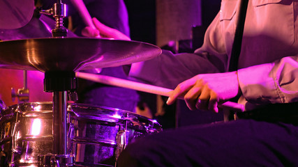 Drummer plays on drum set and cymbal with drumsticks on the stage. Jazz or rock concert performance entertainment. Close up shot with soft selective focus.