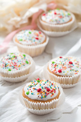 Vanilla cupcakes with white glaze and colorful decorations on light background, selective focus