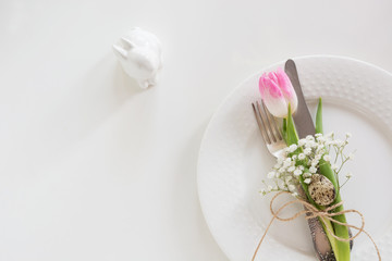 Easter table setting with pink ribbon and tulip on white background. Spring romantic dinner. Top view and copy space for your text.