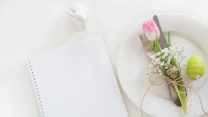 Easter table setting with decor and empty note on white background. Spring romantic dinner. Top view and copy space for your text.