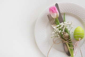 Easter table setting with pink ribbon and tulip on white background. Spring romantic dinner. Top view and copy space for your text.