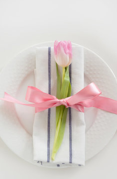 Elegance table setting with pink ribbon and tulip on white background. Spring romantic dinner. Top view.
