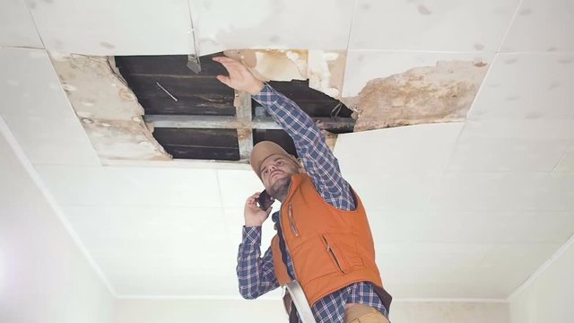 Young man call on the phone in the Service, and public utilities. Ceiling panels damaged huge hole in roof from rainwater leakage.Water damaged ceiling , Insurance case.