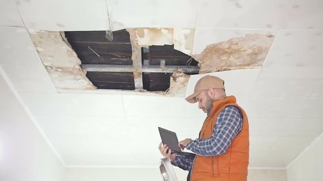 young man makes an emergency inspection of ceiling and use laptop PC. public utilities. Ceiling panels damaged huge hole in roof from rainwater leakage.Water damaged ceiling , Insurance agent.