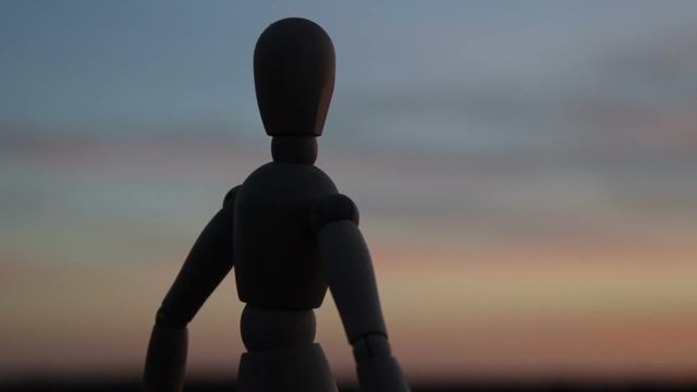 Omino di legno che pensa seduto su un muro di fronte al tramonto.