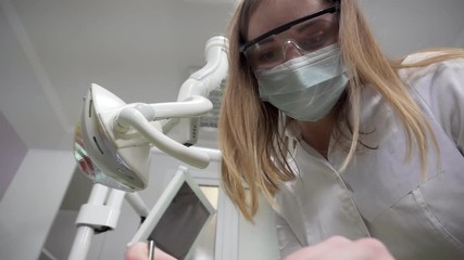 Young female dentist in mask examining patient using tools, Standing Upon a Patient, Looking at Camera, Dentist's Face