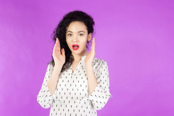 young curly brunette woman surprised, shocked on a pink background