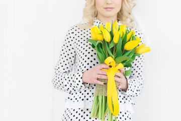Happy young blonde Caucasian woman with yellow tulips in a retro vintage dress