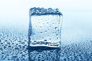Transparent ice cube with reflection on blue glass with water drops