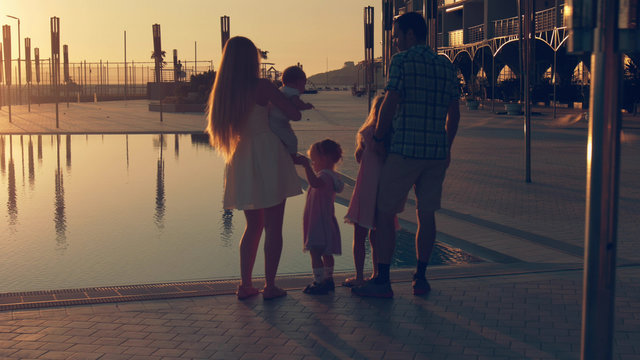 Happy family with three children admiring the sunset reflected in the surface of the pool
