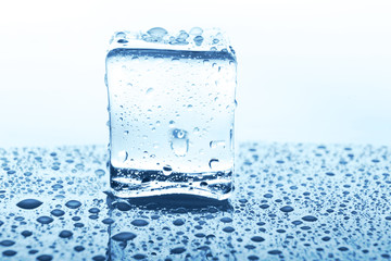 Transparent ice cube with reflection on blue glass with water drops