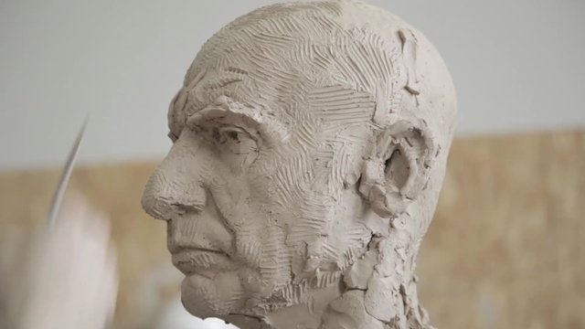 Sculptor modelling sculpture adjusting face details head made of clay. Creative concept.
