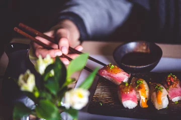 Selbstklebende Fototapeten Mann isst Sushi mit Stäbchen im Restaurant © stockmelnyk