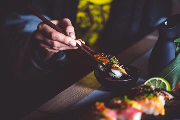 Foto op Canvas Man eating sushi set with chopsticks on restaurant © stockmelnyk