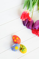 Hand made painted Easter eggs and tulips on white wooden background