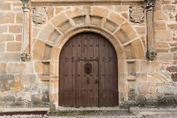 Puerta antigua de madera y fachada con escudos y columnas.
