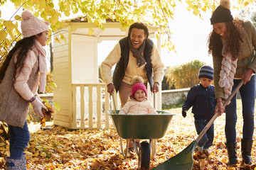 Children Helping Parents To Collect Autumn Leaves In Garden