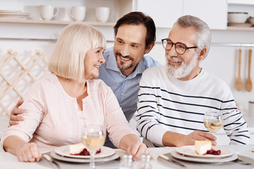 Cheerful mature son hugging elderly parents at home