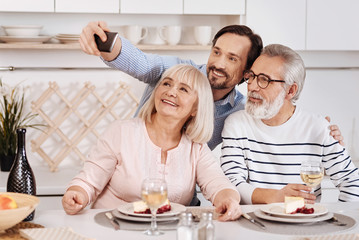 Obraz na płótnie Canvas Joyful mature man taking selfie with aged parents at home