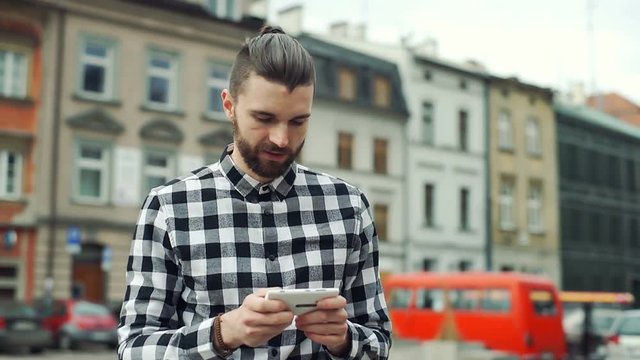 Happy man standing on the square and texting messages on smartphone
