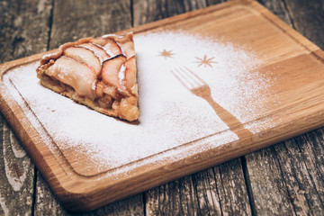 A piece of sliced apple pie with cinnamon on vintage wooden background texture.