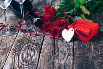 Bouquet of red roses, two glasses, bottle of wine, gift box with tag on vintage wooden board. Valentines day. - Powered by Adobe