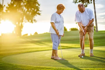 Poster active senior lifestyle, elderly couple playing golf together at sunset © Joshua Resnick