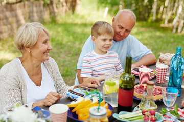 Little boy and his grandparents sitting by Thanksgiving table outdoors