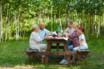 Family sitting by wooden table in natural environment - obrazy, fototapety, plakaty
