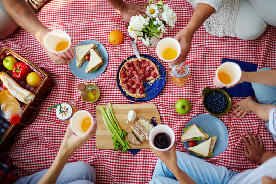 Picnic blanket with healthy food and human hands with drinks over it