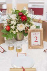 red and ivory floral arrangement prepared for reception, wedding table with candle and setting, winter concept