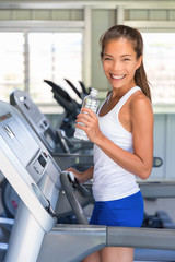 Runner woman drinking water in gym. Asian girl on running treadmill.